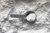 A plastic scoop sits on a pile of powdered creatine