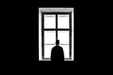 Dark room with a six-panel window in the center and a silouette of a man looking out the window