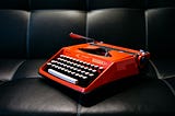 A bright red typewriter sits on a black couch