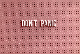 All-caps letters spelling out “Don’t panic” in petal pink on a blush-colored cork board.
