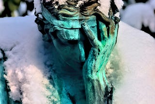 A snow-covered statue of a person with their face in their hands.