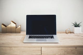 A silver laptop sitting on a wooden desk with a few minimalistic desk items around it.