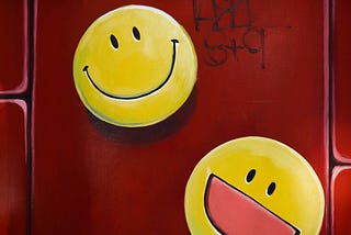 Two yellow smiley faces painted on a red background with graffiti.