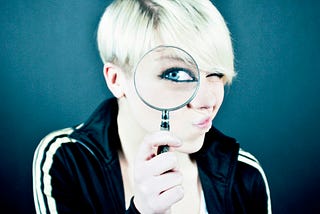 A woman looking out through a magnifying glass with one eye that is magnified.
