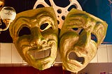Two giant comedy and drama masks hang from a wall