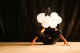 A guy in a balancing yoga position with white balloons over his head.