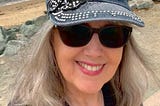 A close-up photo of a woman (the author) in front of the water while wearing sunglasses and a sparkly hat.