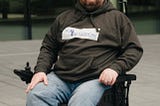 Scott sitting in his wheelchair wearing a grey hoody