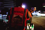 A rickshaw is driving at night through Gulshan circle. The driver’s orange vest, showing the “Gulshan-453” sign, allows him to circulate in the protected area.