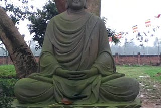 Cement statue of Buddha sitting cross-legged.