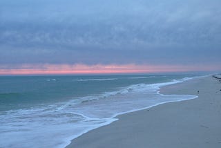 Waves on the sand, with dusky clouds and a pink stripe in the sky