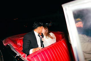A man and a woman kissing in a red convertible