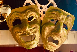 Two giant comedy and drama masks hang from a wall