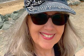 A close-up photo of a woman (the author) in front of the water while wearing sunglasses and a sparkly hat.
