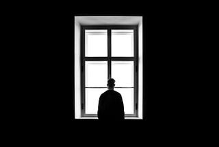 Man standing before fully lit window, with background in black and the man silhouetted against the light