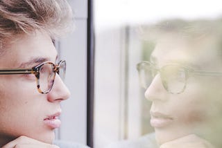 A young man looking at his reflection in a window.