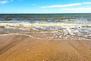 A Gulf Coast beach on a sunny day, with waves lapping at the sand.