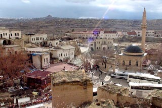 Cappadocian village with a mosque and white buses waiting for the tourists.