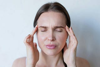 A woman rubbing her temples trying to soothe her migraine headache.