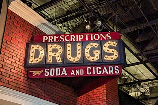 Store sign reading Prescriptions, DRUGS, Soda and Cigars. That isn’t even close to the worst of it