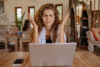 A frustrated woman throws up her hands while looking at her laptop.
