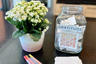 Gratitude jar, colorful pens, paper and flowers on kitchen counter