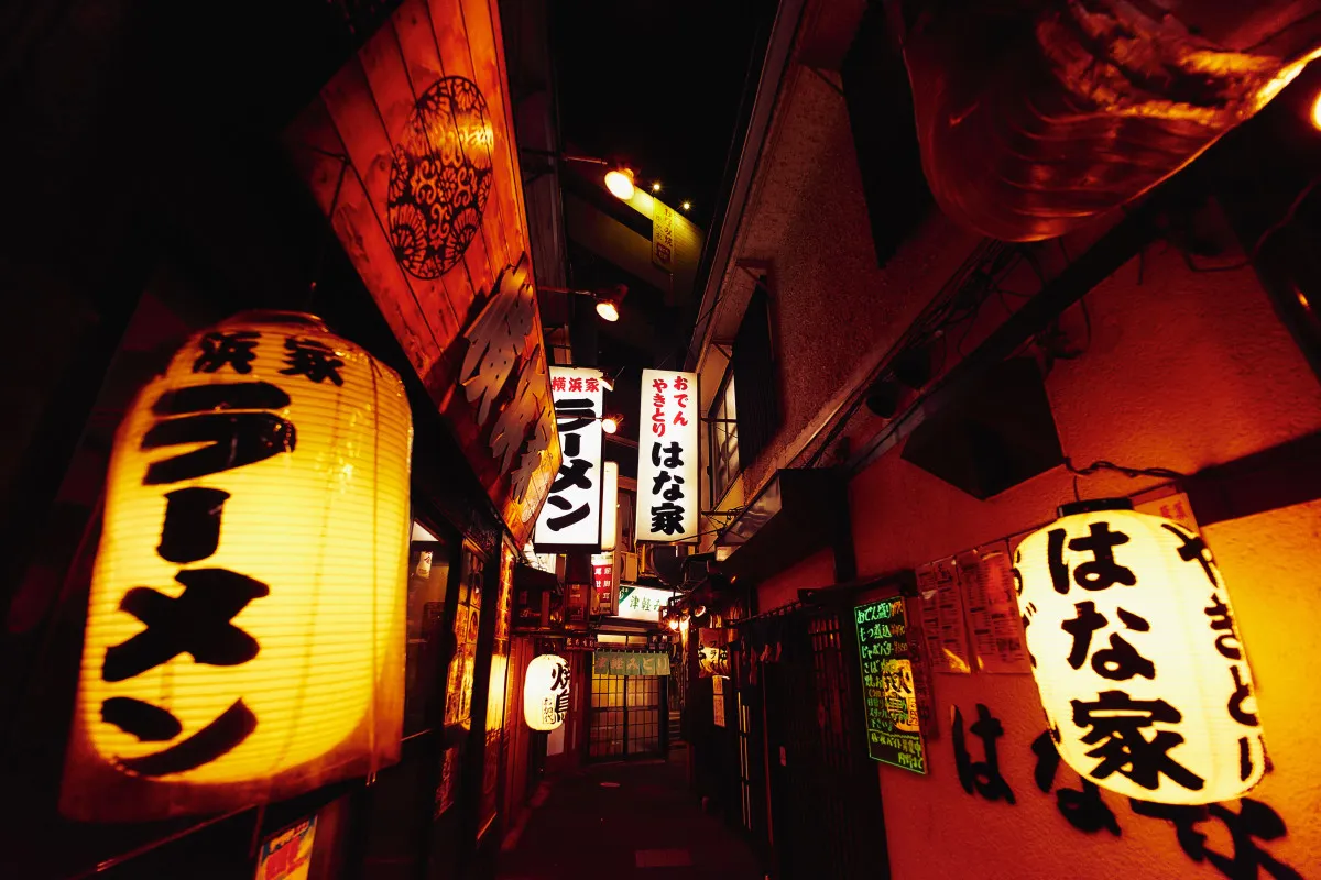 Glowing lanterns hang in a small alleyway in Tokyo at night.