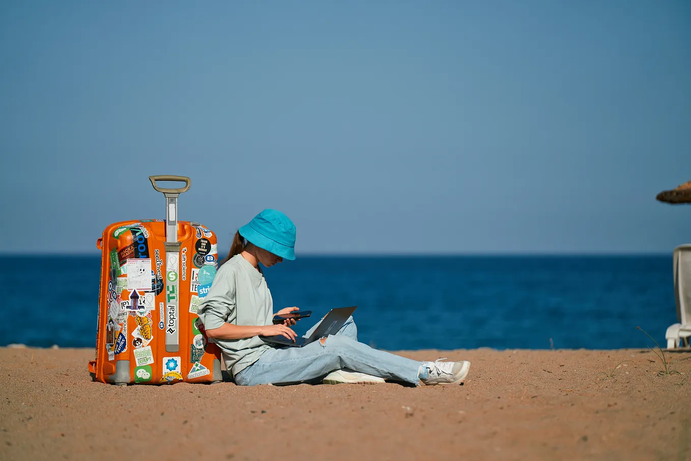 A girl by the beach with a suitcase and laptop.