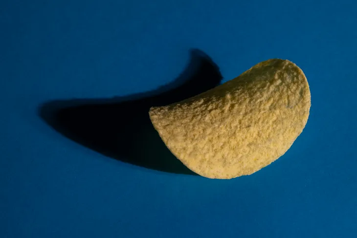 A single Pringles potato chip, a highly processed food. Dark blue background.