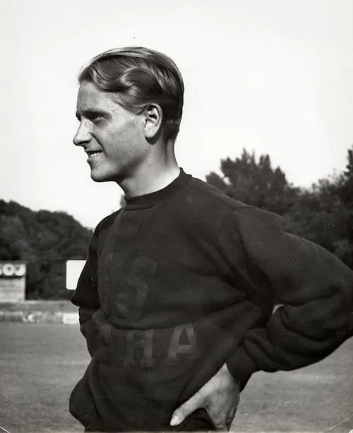 Zdeněk Koubek, standing on a sports field, wearing an athletic shirt, smiling, hands on his hips