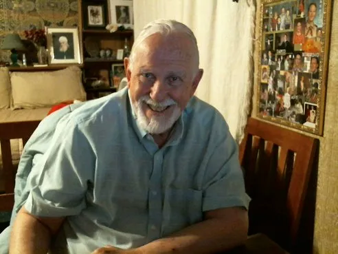 A smiling face, white hair and beard. Light blue shirt.