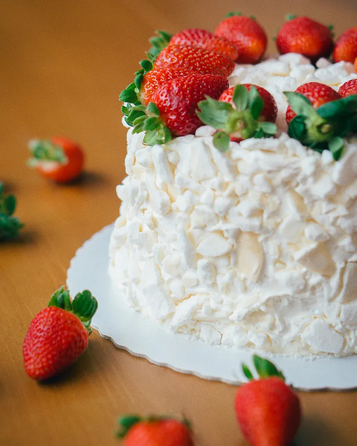 A close-up of a cake covered in white frosting and topped with fresh strawberries