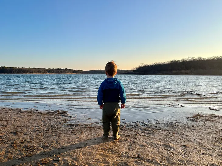 Little boy looking out on the fresh, green breast of his hometown lake.